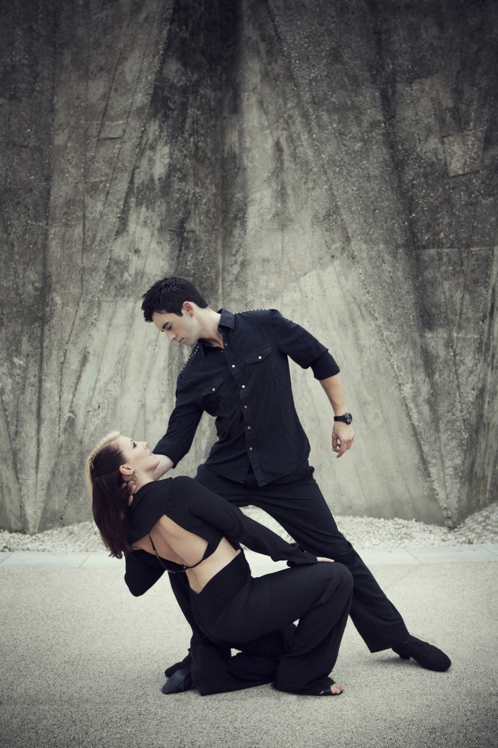 Jordan and Tatiana in a partnered dance pose against a concrete wall